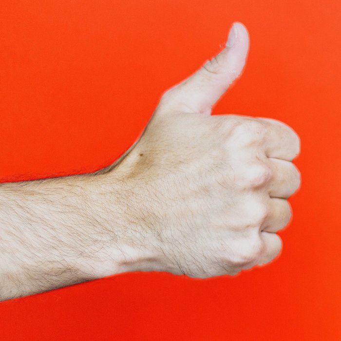 Hand vor orangefarbenem Hintergrund zeigt Daumen nach oben